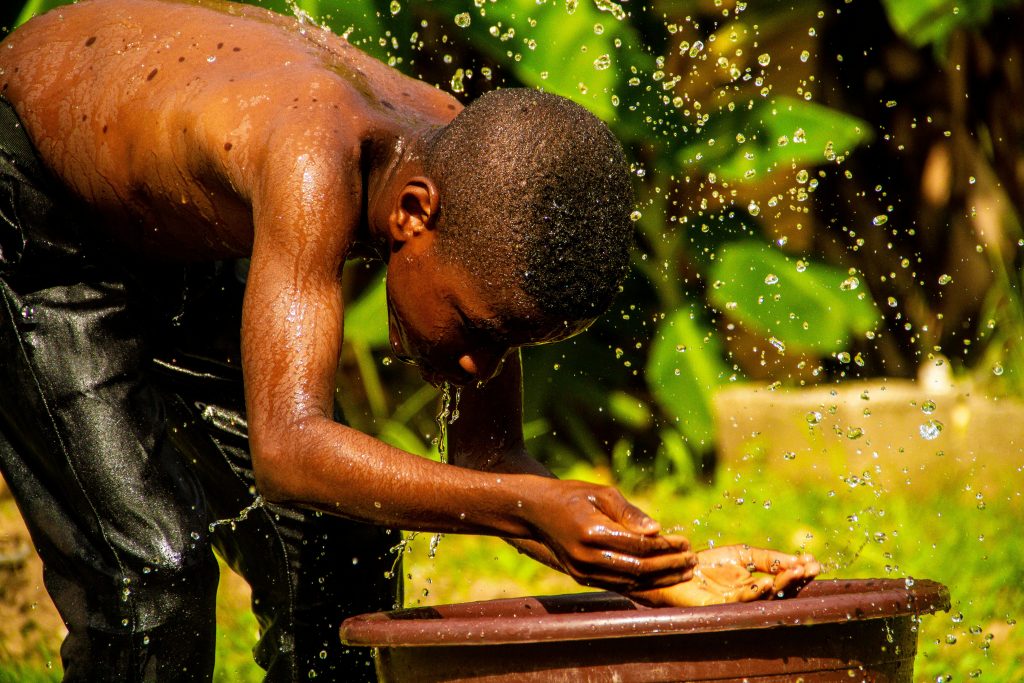 A young boy splashes water on himself outdoors in a refreshing and playful moment.