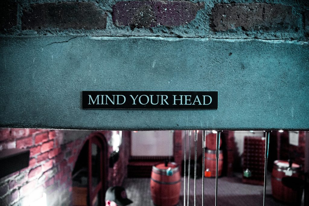 A 'Mind Your Head' sign in a rustic brick barrel cellar setting, creating a safety awareness ambiance.