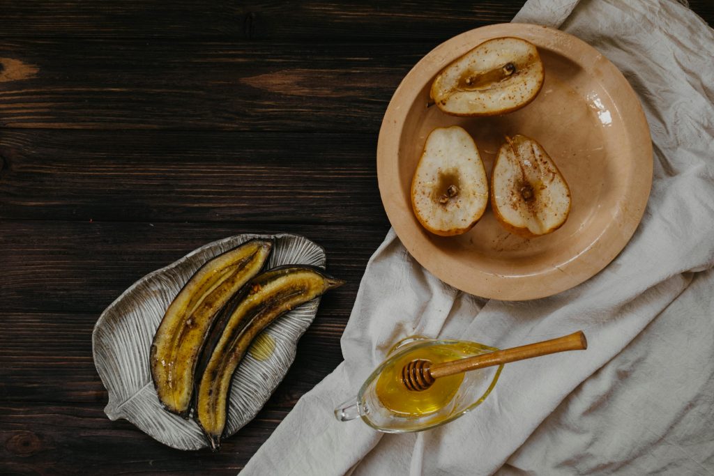 A rustic breakfast setup featuring baked pears, banana slices, and honey on a wooden table.