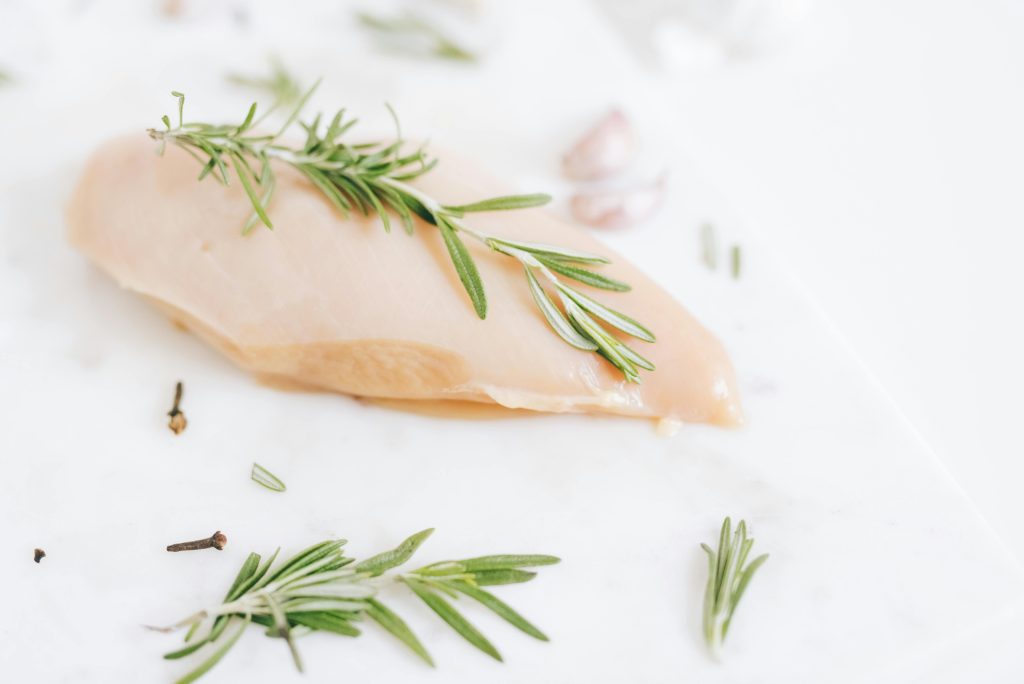 Healthy raw chicken breast garnished with rosemary on a marble surface.