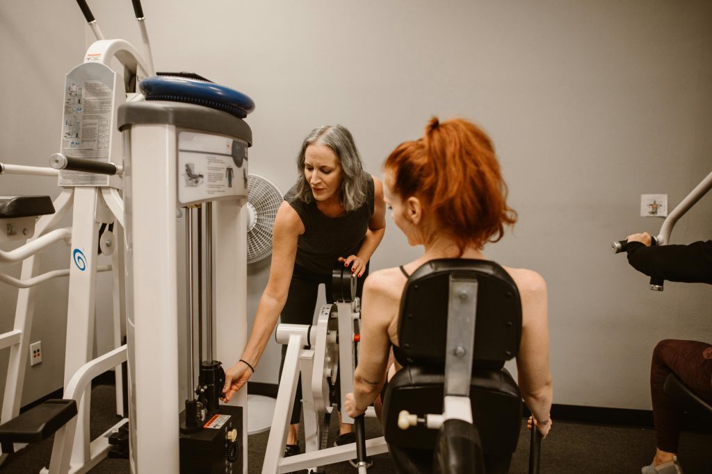 A personal trainer guides a woman using gym equipment, promoting healthy living.